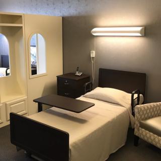 A hospital room featuring a bed, side table, and chair under soft lighting.