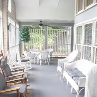 A cozy enclosed porch with comfortable seating, including wicker furniture and rocking chairs, offering a bright and relaxing atmosphere.