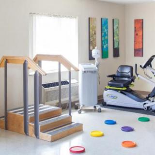 A rehabilitation room equipped with exercise gear for physical therapy, including a staircase trainer and colorful floor markers.