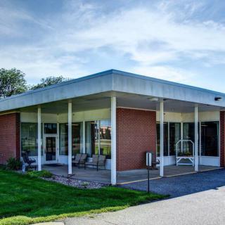A modern building with large windows and a flat roof, surrounded by grass and trees under a blue sky.