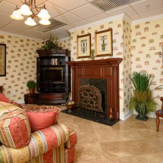 A cozy living room with traditional decor featuring a fireplace, patterned wallpaper, and comfortable seating.