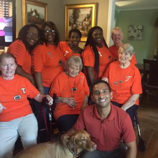A group of people wearing orange shirts pose together indoors, with a dog in front.