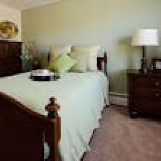 A cozy bedroom with a wooden bed frame, soft green bedding, and bedside tables topped with a lamp.