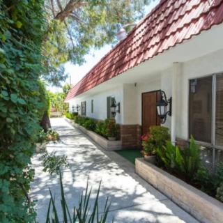A sunny walkway lined with greenery and a building featuring red roof tiles and decorative lanterns.