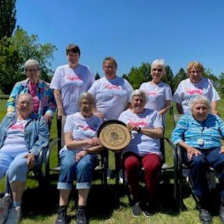 A group of women outdoors posing with an award on a sunny day.