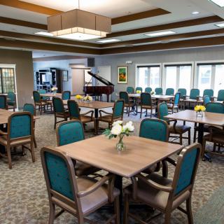 A spacious dining area with neatly arranged tables and chairs, featuring a piano in the background.