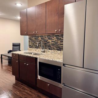 A modern kitchen with wooden cabinets, stainless steel refrigerator, and stone backsplash.