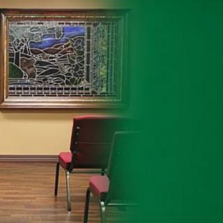A room with a stained glass artwork on the wall, featuring red chairs and a wooden floor.