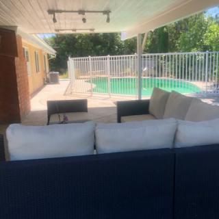 A comfortable patio area with a sofa, overlooking a fenced swimming pool in the backyard.
