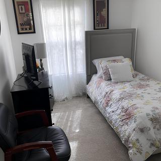 A cozy single bedroom with a floral duvet, featuring a television and an armchair.