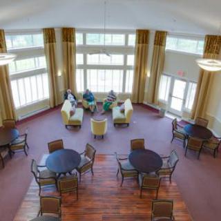 A spacious lounge area with large windows, featuring multiple seating arrangements with tables and chairs.