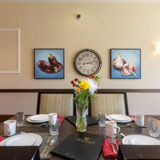 A well-set dining table with a vase of flowers and a wall clock in the background.