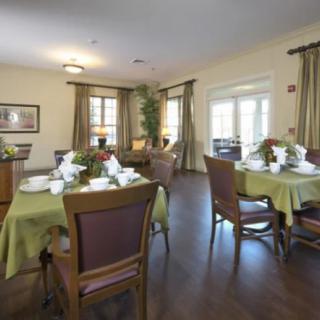A well-decorated dining room with neatly set tables and chairs, featuring large windows and elegant curtains.