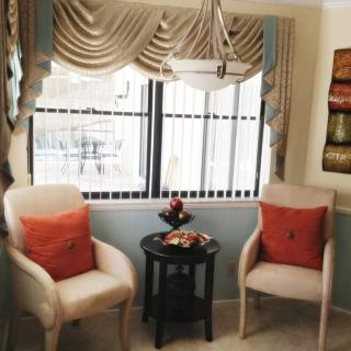 A cozy seating area with two chairs and a small table by the window, featuring elegant curtains and decorative cushions.
