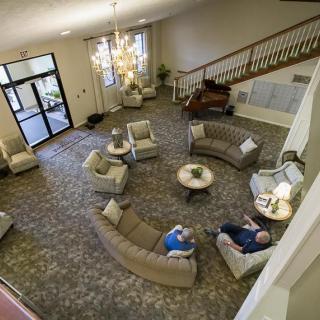 A spacious lobby with a seating area, featuring sofas and armchairs, illuminated by a large chandelier and accompanied by a staircase.