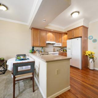 A cozy kitchen and dining area with wooden cabinets, a refrigerator, and a small dining table adorned with flowers.
