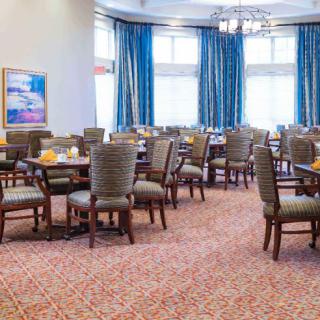 An empty dining room with neatly arranged tables and chairs, featuring large windows and blue curtains.