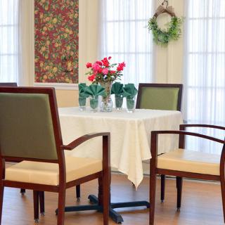 A cozy dining area with a neatly set table, surrounded by chairs and decorated with flowers and a wreath.