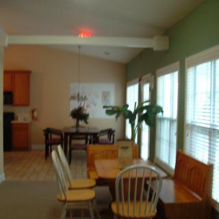 A cozy dining room area adjacent to a kitchen, featuring a wooden table with chairs and large windows letting in natural light.