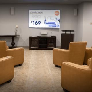 A conference room setup with comfortable chairs facing a projector screen displaying a presentation.