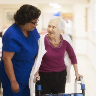 A nurse assists an elderly woman using a walker in a healthcare setting.