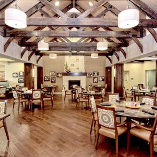A spacious and elegantly designed dining room with wooden floors, ceiling beams, and well-arranged tables and chairs.
