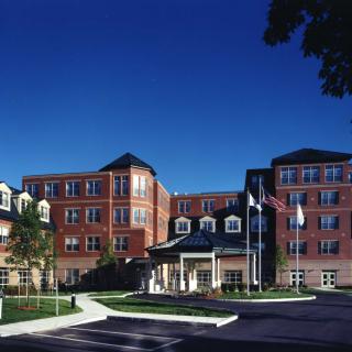 A large brick hospital building with multiple floors and a welcoming entrance under a clear blue sky.