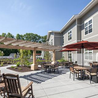A sunny outdoor patio area with tables, chairs, and a pergola next to a modern building.