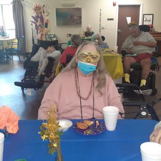 An elderly person enjoying a meal at a community gathering, surrounded by colorful decorations and others in the background.