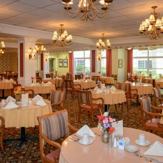 An elegant dining room with round tables set for guests, featuring chandeliers and classic decor.