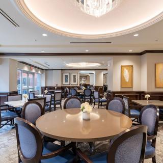 An elegant dining area with round tables, upholstered chairs, and a chandelier overhead.