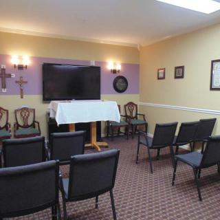 A small chapel room with arranged chairs, a television, and religious symbols on the wall.