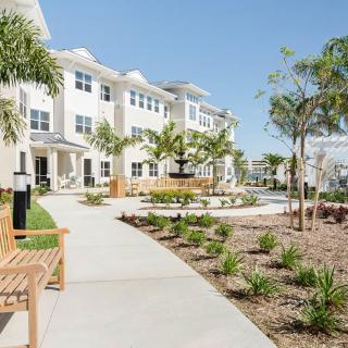 A modern residential building with landscaped pathways and benches surrounded by tropical plants.