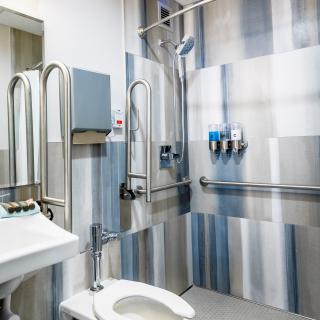 A well-equipped accessible bathroom featuring handrails, a toilet, sink, and shower.