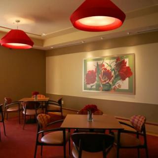 A cozy restaurant interior featuring red lighting, artwork on the wall, and neatly arranged tables and chairs.