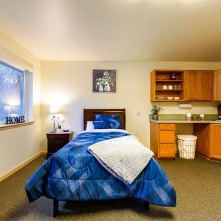 A cozy bedroom with a single bed and a kitchenette.