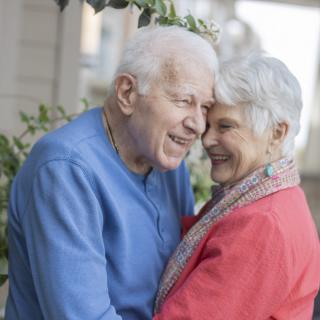 An elderly couple sharing a joyful embrace outside.