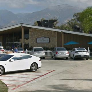 A modern commercial building with a parking lot filled with various cars, set against a backdrop of mountains.