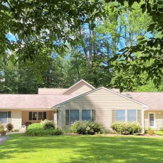 A one-story house with a well-maintained lawn and surrounded by trees on a sunny day.