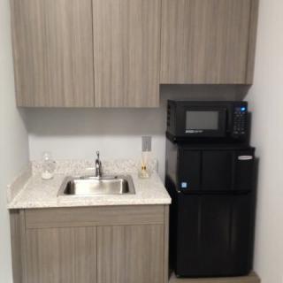 Small kitchenette setup with sink, cabinets, microwave, and a water dispenser.