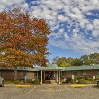 A building with an entrance, surrounded by autumn trees and a cloudy sky.