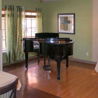A grand piano in a cozy living room with green walls and hardwood flooring.