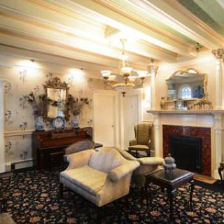 A vintage-style living room with elegant furniture, wallpaper, and a cozy fireplace.