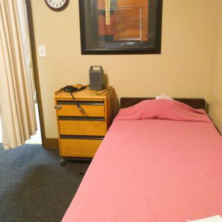 A simple bedroom setup featuring a single bed with pink bedding, a nightstand, and wall art.