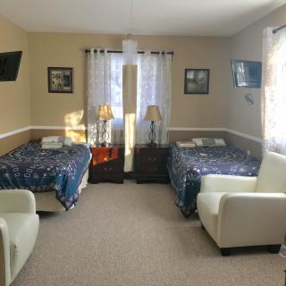 A cozy bedroom with two beds, each accompanied by a chair and television, illuminated by natural light through the window.