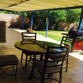 A sunny backyard patio with a shaded dining area featuring a round table and chairs.