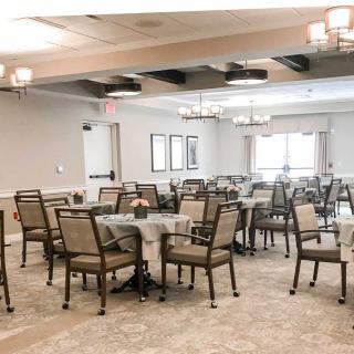 An elegant banquet room with neatly arranged tables and chairs, featuring soft lighting and large windows.