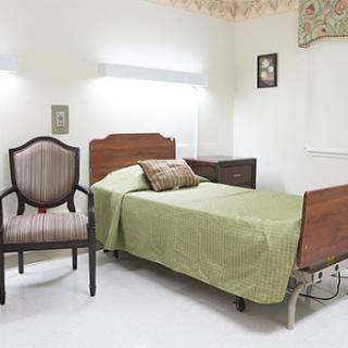A simple and serene bedroom setup featuring a bed with a green coverlet and an elegant chair.