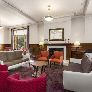 A cozy living room with sofas and chairs arranged around a central coffee table, featuring a warm fireplace under a large mirror.