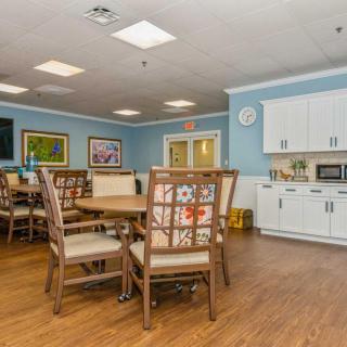 A cozy dining area with wooden tables and chairs, featuring a kitchenette in the background.